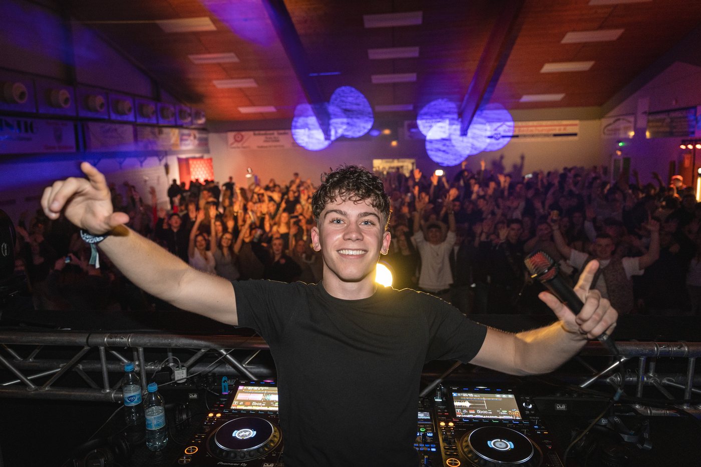 DJ Haemmer lacht in die Kamera vor einem tanzenden Saal voller Gäste