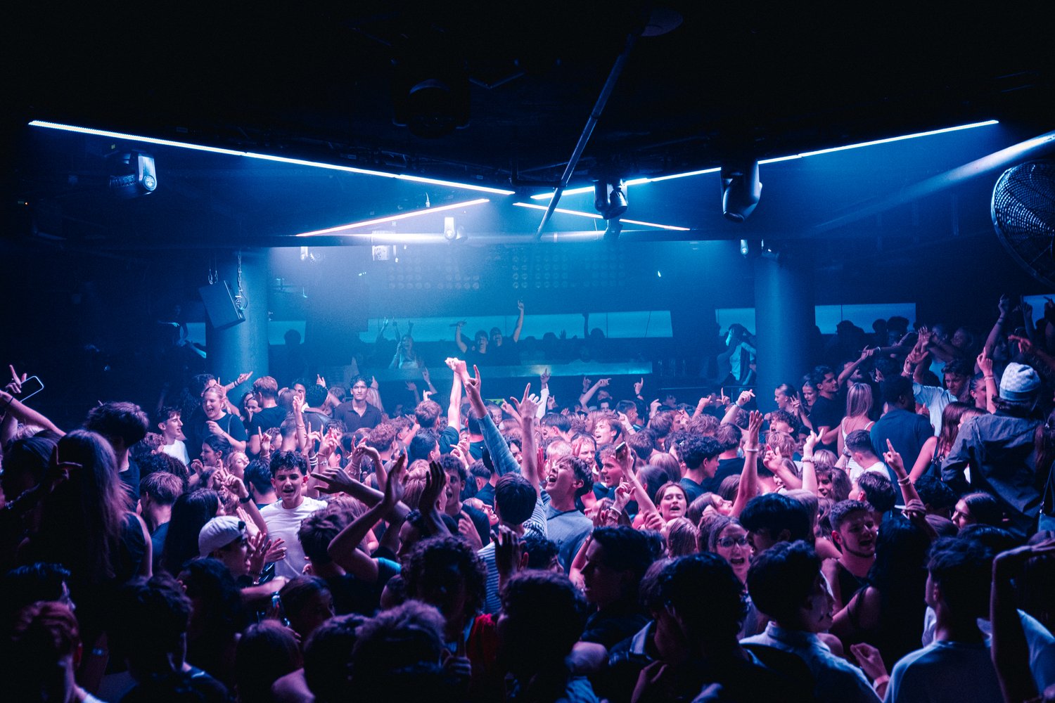 Voller Club mit leuchtender DJ-Bühne und tanzender Menge
