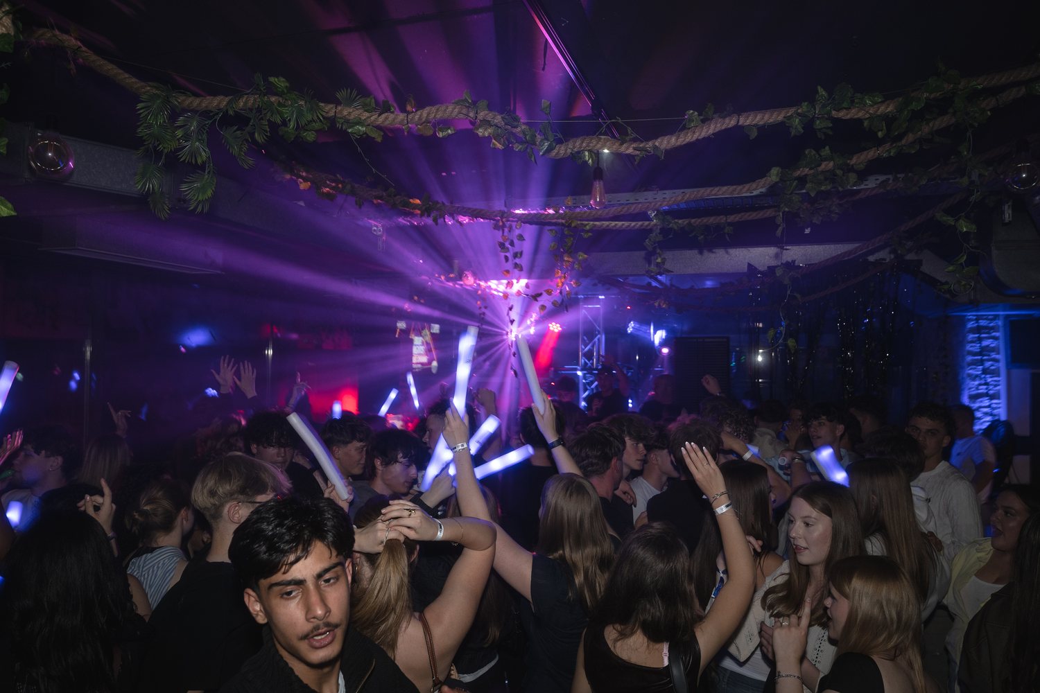 Feiernde Menge mit Leuchtstäben unter lila Lichtshow